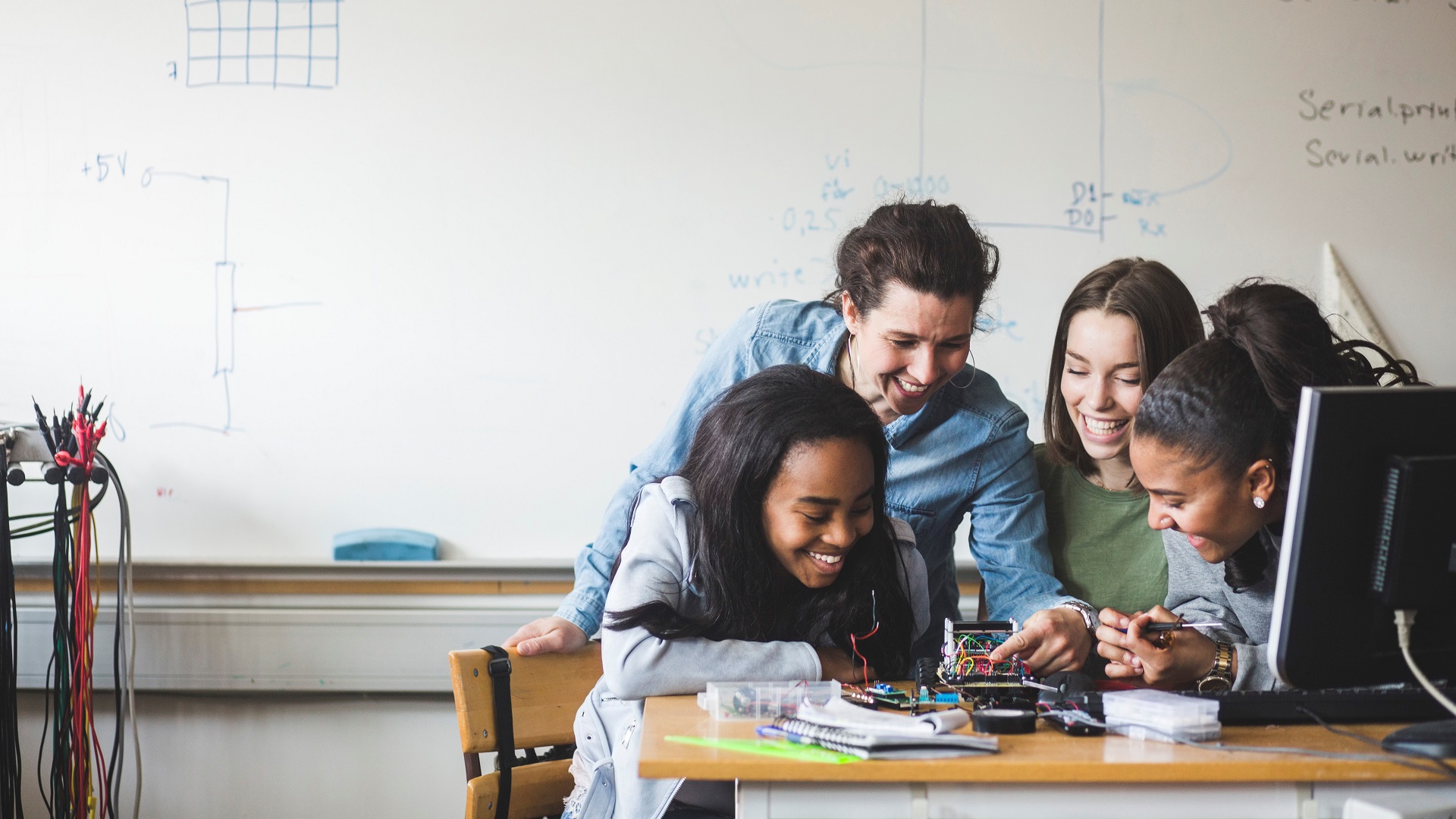 Smiling female teacher and high school teenage students preparing robot on desk in classroom